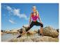 Femme en haut de sport fuchsia et legging noir s'étirant sur des rochers à la plage.