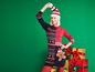 Une femme portant un pull de Noël avec un motif d'homme en pain d'épices se tient à côté de cadeaux.