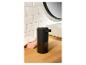 Un distributeur de savon automatique noir sur un comptoir en bois dans une salle de bain.