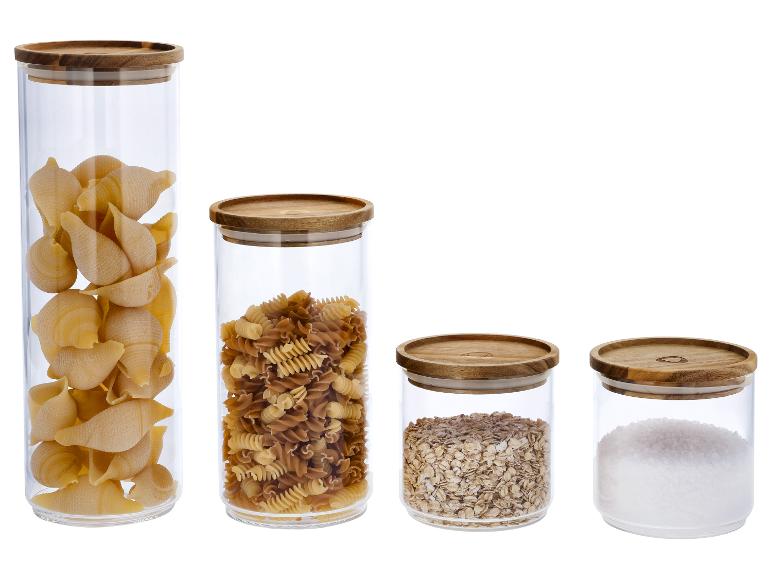 Quatre bocaux en verre avec couvercles en bois, contenant des pâtes, de l'avoine et du sel.