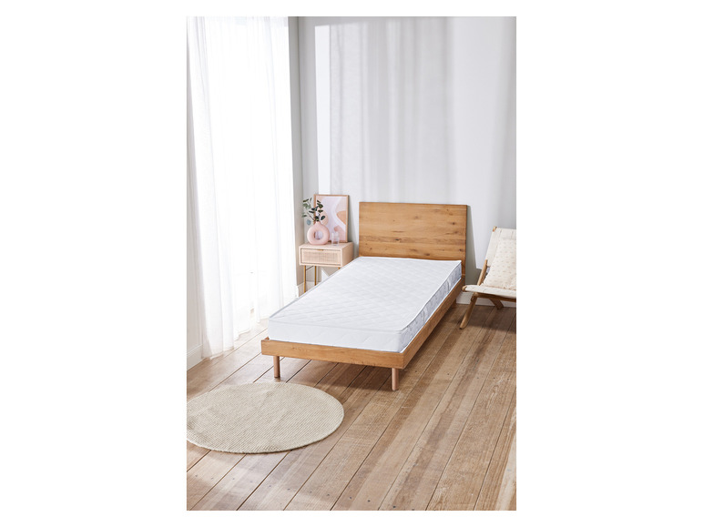 Un matelas blanc sur un cadre de lit en bois dans une chambre claire.
