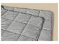 Gros plan d'une couverture matelassée grise douce avec une texture moelleuse sur fond beige.