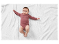 Un bébé dans un body rose sur une couverture blanche en tricot.