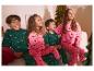 Quatre enfants en pyjamas festifs, deux en vert avec des voitures et deux en rose avec des teckels, regardant un sapin de Noël.