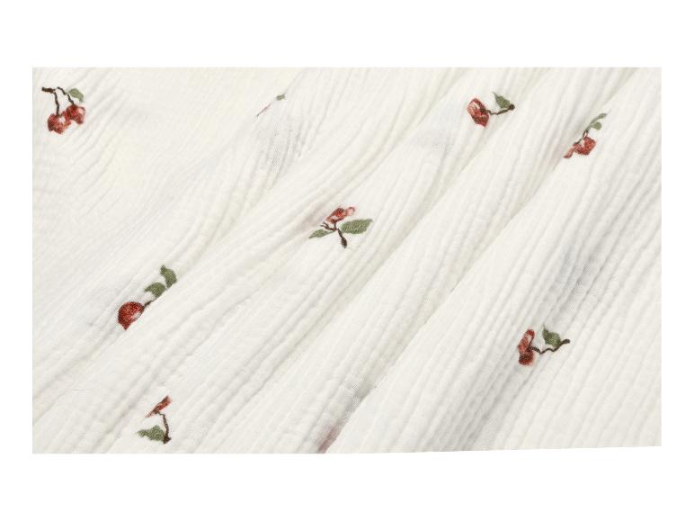 Tissu blanc froissé avec des cerises brodées.