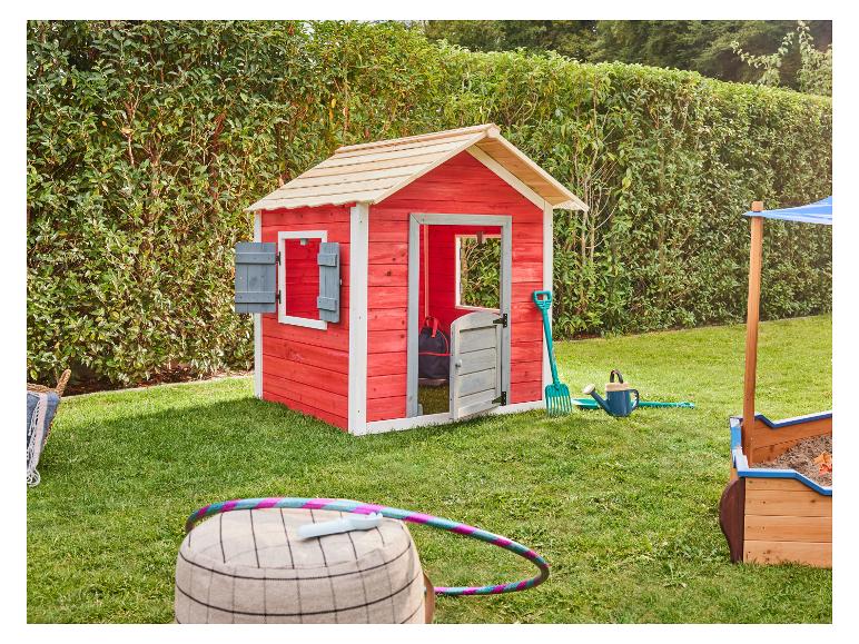 Maisonnette de jeu en bois rouge avec bac à sable et jouets d'extérieur dans un jardin vert.