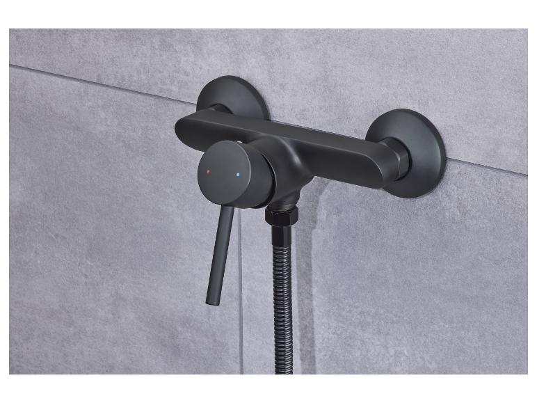 Un mitigeur de douche noir avec un bouton de thermostat sur un mur en carrelage gris.