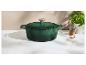 Cocotte en fonte verte sur un comptoir en marbre avec des herbes.