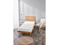 Un matelas blanc sur un sommier en bois avec un tapis rond en jute.