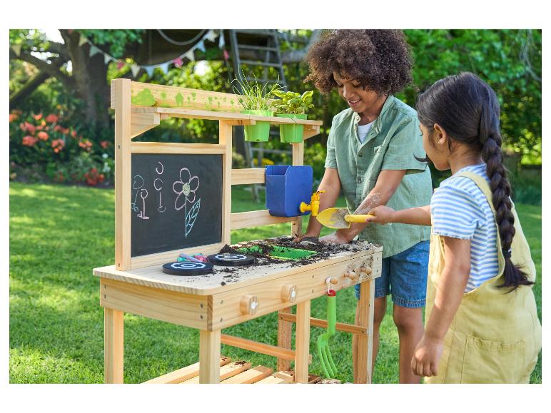 Enfants jouant avec une cuisine de boue en bois dans un jardin.