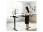 Femme debout devant un bureau noir réglable en hauteur avec moniteur et ordinateur portable.