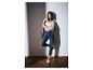 Femme en jean, top blanc et veste vert clair, appuyée contre un mur.