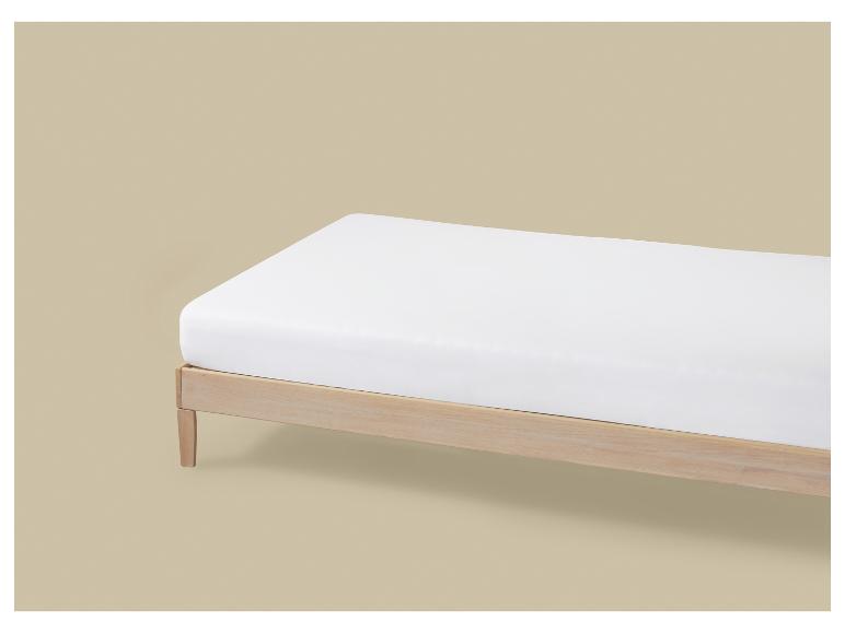Un matelas blanc sur un cadre de lit en bois sur fond beige.