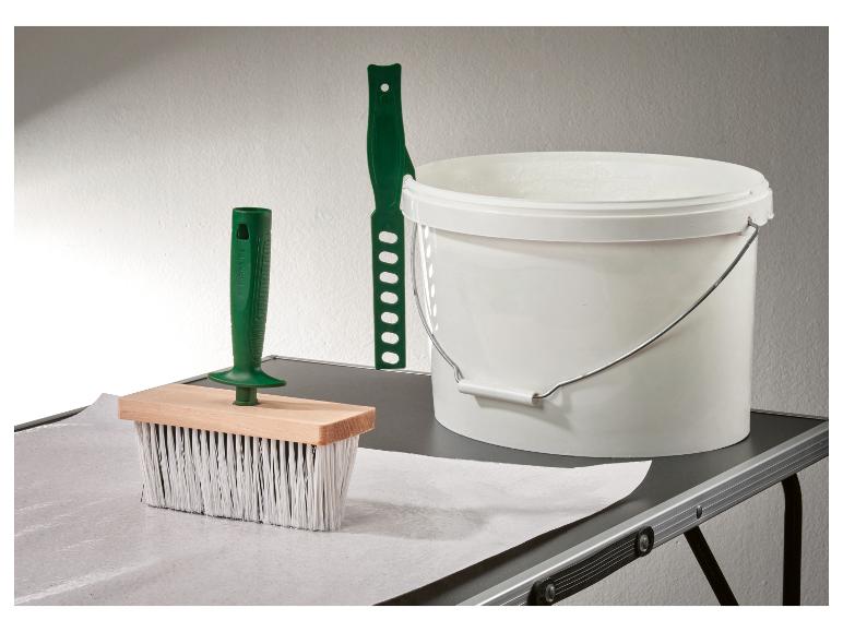 Outils de tapisserie: brosse, spatule et seau de colle sur une table.