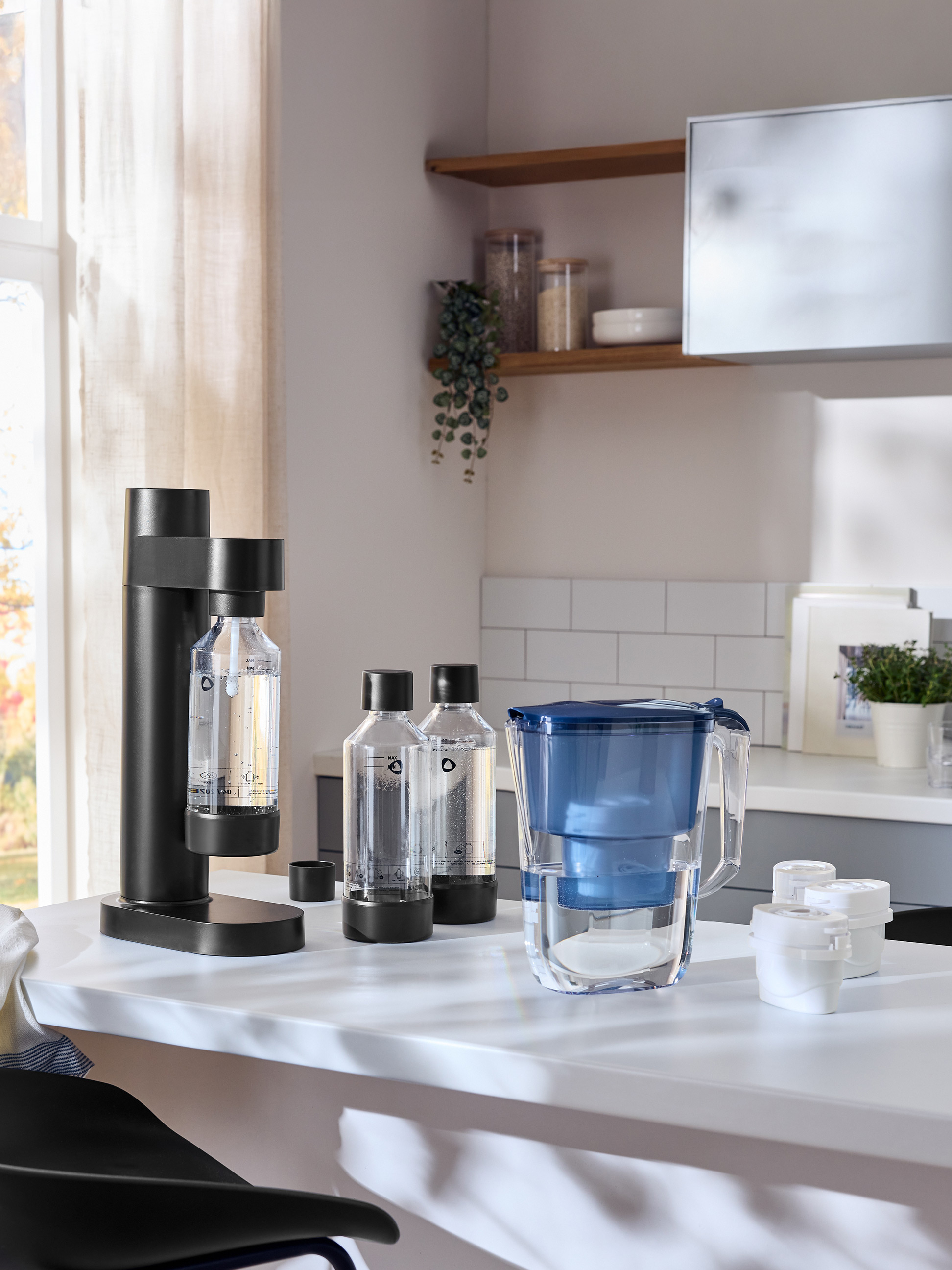 Machine à eau pétillante noire avec bouteilles et carafe filtrante bleue sur un comptoir blanc.