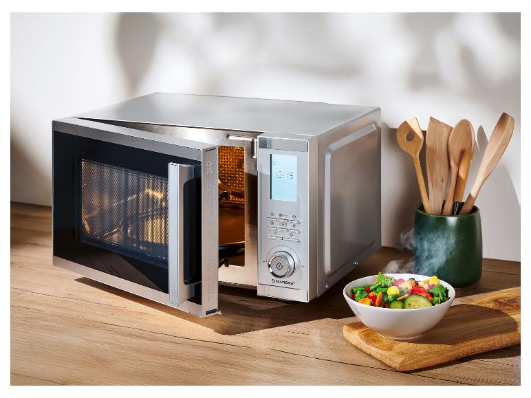 Micro-ondes argenté avec porte ouverte et un bol de légumes sur une planche en bois.