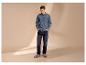 Homme en chemise et jean en denim, les mains dans les poches, regardant vers le bas.