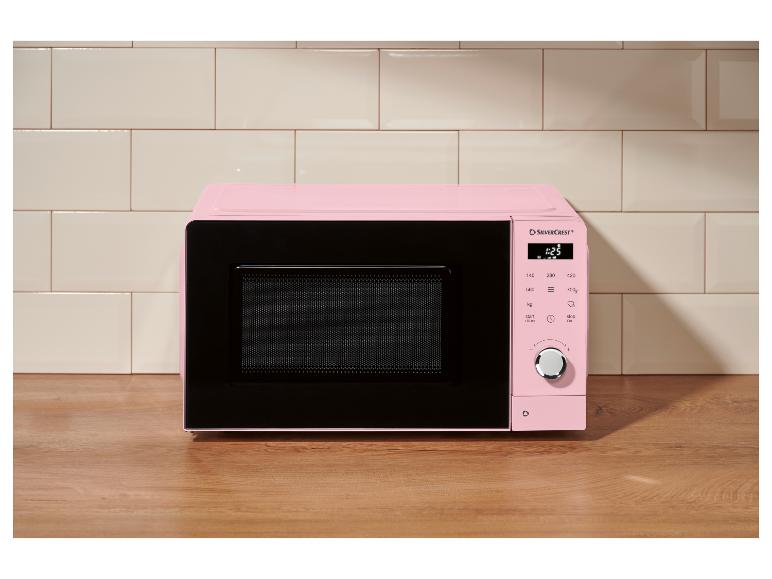 Micro-ondes rose avec panneau de commande numérique sur un comptoir en bois, devant des carreaux de cuisine.