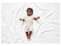 Un bébé dans un body blanc à pois sur une couverture blanche.