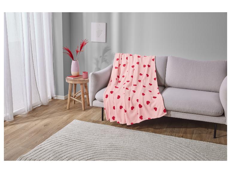 Une couverture en polaire rose avec des cœurs rouges sur un canapé gris.