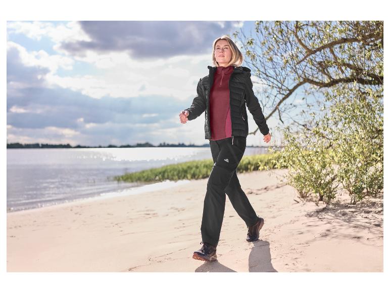 Femme portant un t-shirt technique bordeaux CRIVIT marchant sur une plage de sable.
