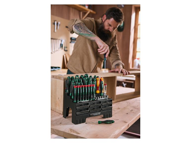 Un homme utilise un tournevis d'un grand ensemble de tournevis et d'embouts sur un établi en bois.