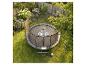 Enfant sur un trampoline avec filet de sécurité dans un jardin fleuri avec une clôture en bois.