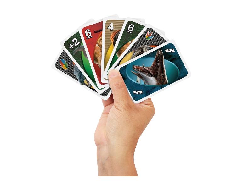 Une main tient un jeu de cartes UNO sur le thème des dinosaures.