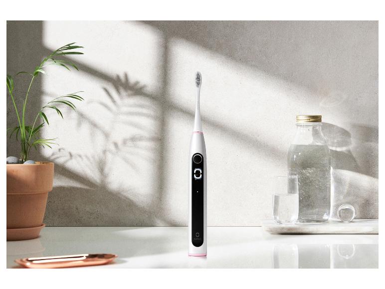 Une brosse à dents électrique Oclean, un verre et une bouteille d'eau.