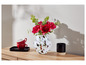 Un vase blanc avec des fleurs roses et des tasses rouges sur une table en bois.