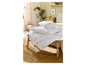 Oreillers et couette blancs empilés sur une table en bois dans une chambre.