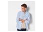 Homme en chemise bleue et t-shirt beige, bras croisés, regardant sur le côté.