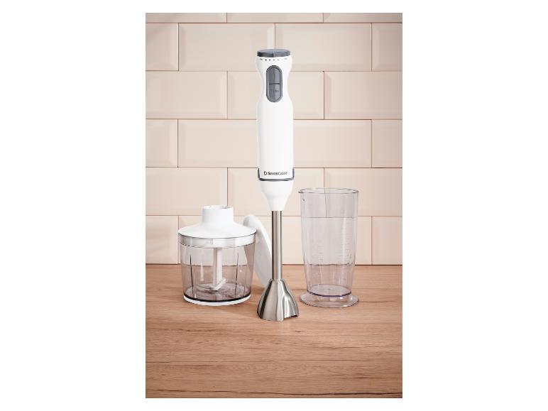 Mixeur plongeant blanc avec accessoire hachoir et verre doseur sur une surface en bois.