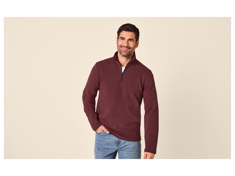 Homme portant un pull bordeaux à fermeture éclair et un jean.