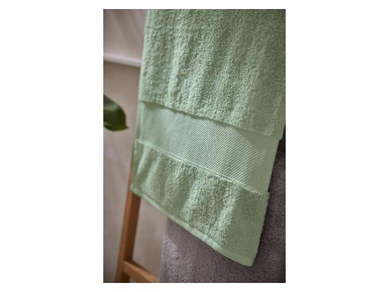 Serviette vert clair avec une bande texturée, suspendue à une échelle en bois dans une salle de bain.