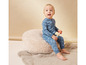 Un bébé assis sur un coussin moelleux, vêtu d'une combinaison bleue à motifs de nuages.