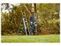 Homme avec casque de protection et tronçonneuse, à côté d'une échelle, taillant des arbres.