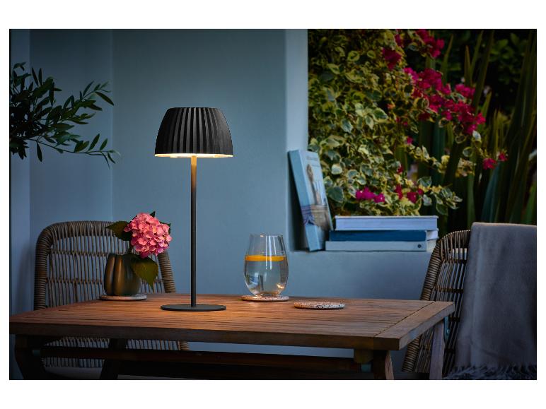 Lampe de table sur une table en bois avec des fleurs et une boisson sur une terrasse.
