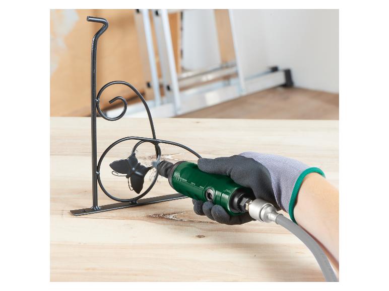 Main gantée utilisant un outil rotatif vert pour poncer un support métallique noir.