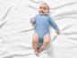 Un bébé dans un body bleu sur une couverture blanche.