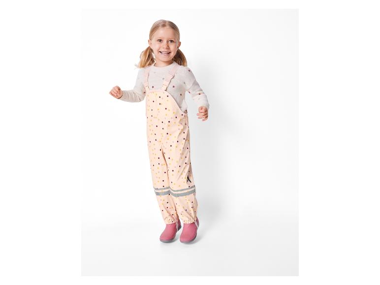 Une fillette saute avec un imperméable et des bottes roses.