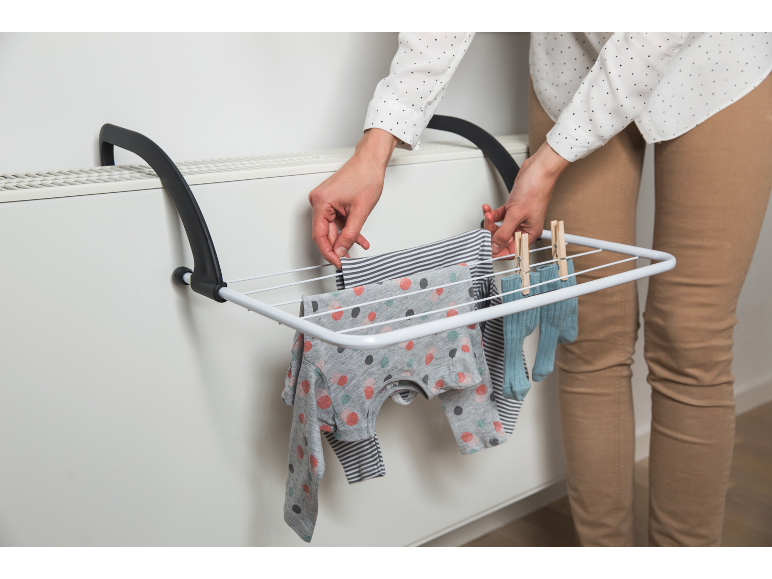 Femme étendant des vêtements de bébé sur un séchoir fixé à un radiateur.