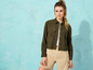 Une femme portant une chemise verte et un short beige, devant un fond bleu.