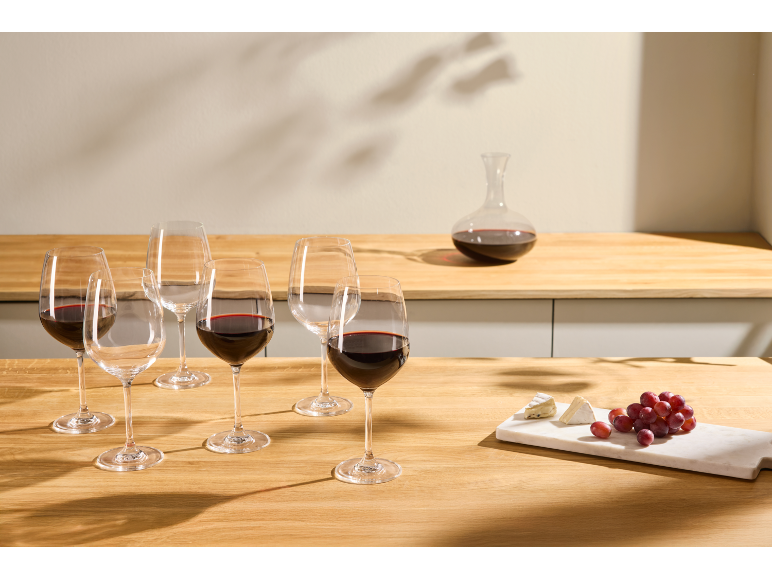 Verres à vin, carafe, fromage et raisins sur une table en bois.