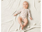 Un bébé dans un body blanc à imprimé floral, allongé sur une couverture tricotée.