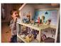 Une petite fille joue avec une maison de poupée en bois avec des meubles et des figurines.