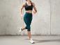 Femme en soutien-gorge de sport noir et capri vert en train de courir.