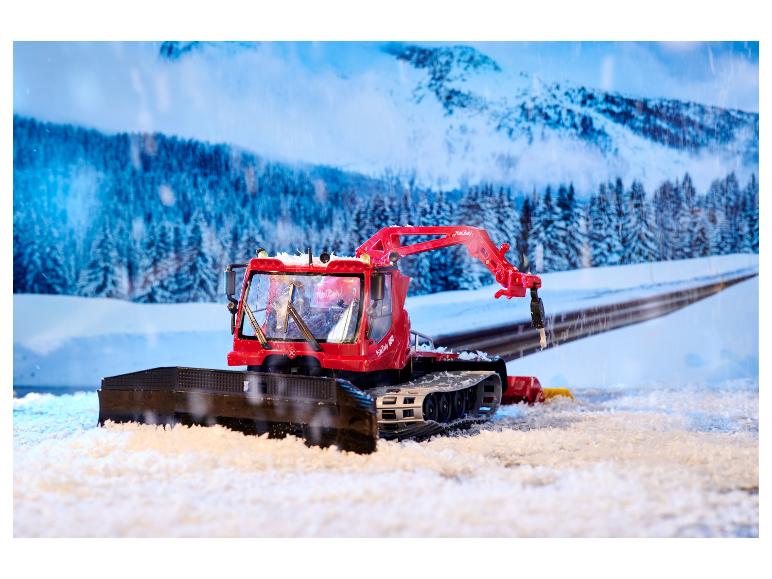 Dameuse PistenBully 600 rouge avec chasse-neige dans un paysage hivernal.