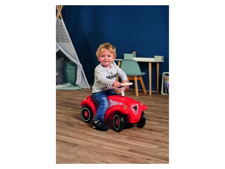 Petit garçon sur un porteur rouge dans une chambre d'enfant.