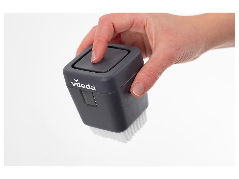 Une main tient une brosse de nettoyage grise avec des poils blancs, appuyant sur le bouton.